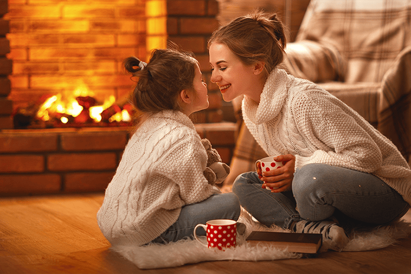 Mother sitting with daughter near warm fire, enjoying their home's indoor air quality.